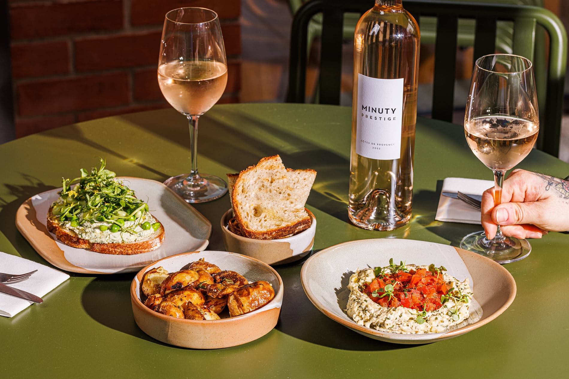 A sunlit table outside Feels Like June bears rose wine, roast potatoes and delicious avocado toast.