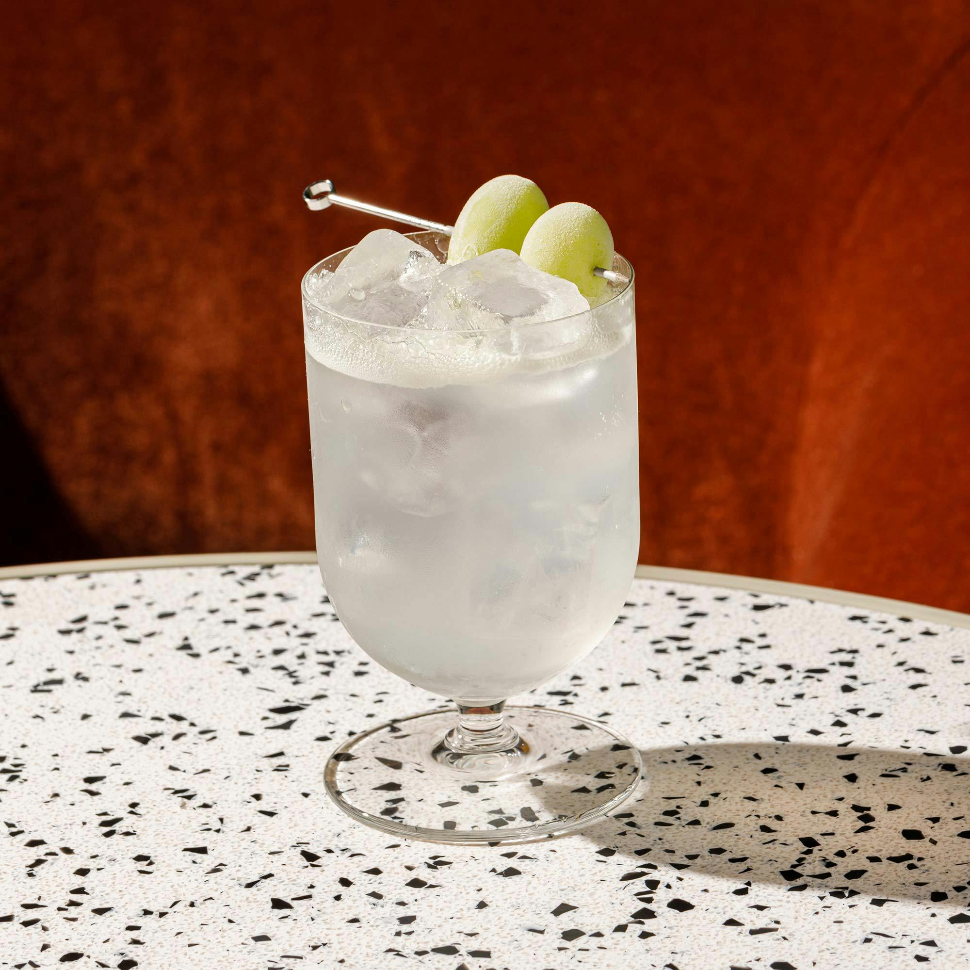 A tall iced cocktail with olives.